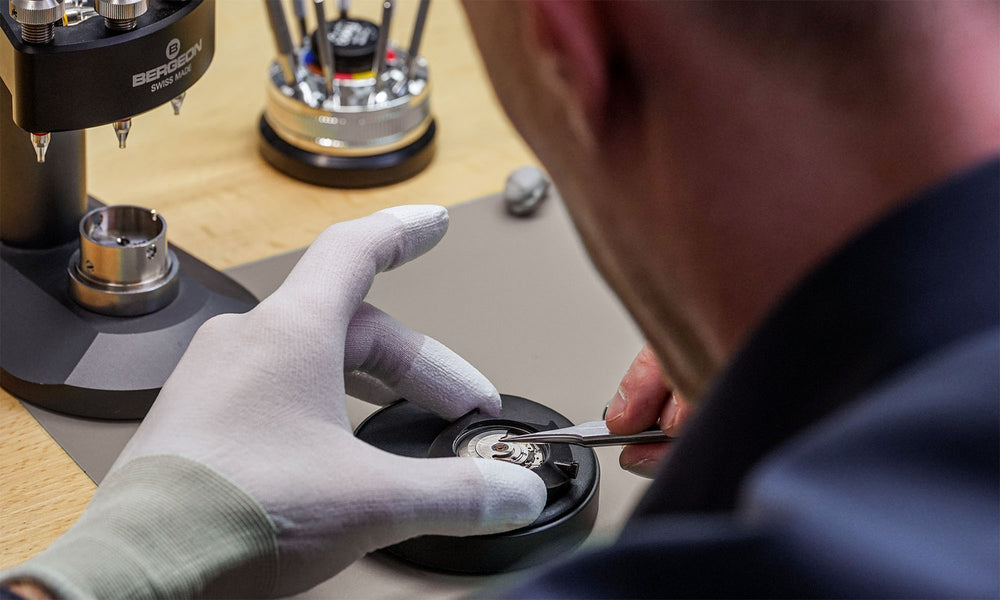 The picture shows the master watchmaker assembling an automatic watch. Here, the movement is inserted into the watch. This is followed by quality control.