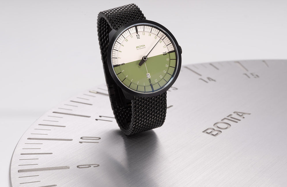 A UNO 24 One hand 24 Hour watch standing on a Botta wall clock