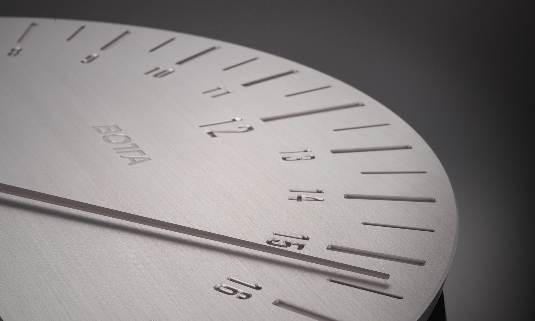 Detailaufnahme der UNO 24 Slate Industrial Designwanduhr von BOTTA: Das Bild zeigt das minimalistische Zifferblatt aus gebürstetem Edelstahl mit klar gravierten Stundenmarkierungen von 8 bis 17 und einem markanten Einzelzeiger. Diese 24-Stunden Wanduhr im Schieferdesign verbindet industrielle Klarheit mit präziser Zeitwahrnehmung. Eine exklusive Designwanduhr – jetzt kaufen oder bestellen für modernes Wohnen