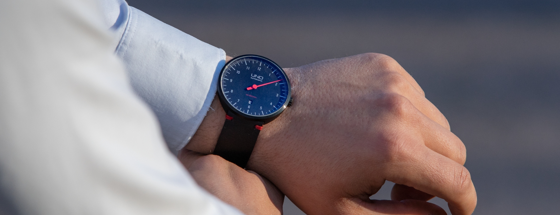 Das Bild zeigt die BOTTA UNO 35 Edition als Automatikuhr am Handgelenk. Die Einzeigeruhr besitzt ein tiefblaues Zifferblatt mit markantem roten Zeiger und roten Akzenten am Lederband. Diese Designuhr verbindet minimalistisches Bauhaus-Design mit präzisem Swiss-Made Sellita SW200-1 Automatikwerk. Eine hochwertige Armbanduhr für Individualisten, die eine exklusive Uhr mit einem Zeiger kaufen oder bestellen möchten.