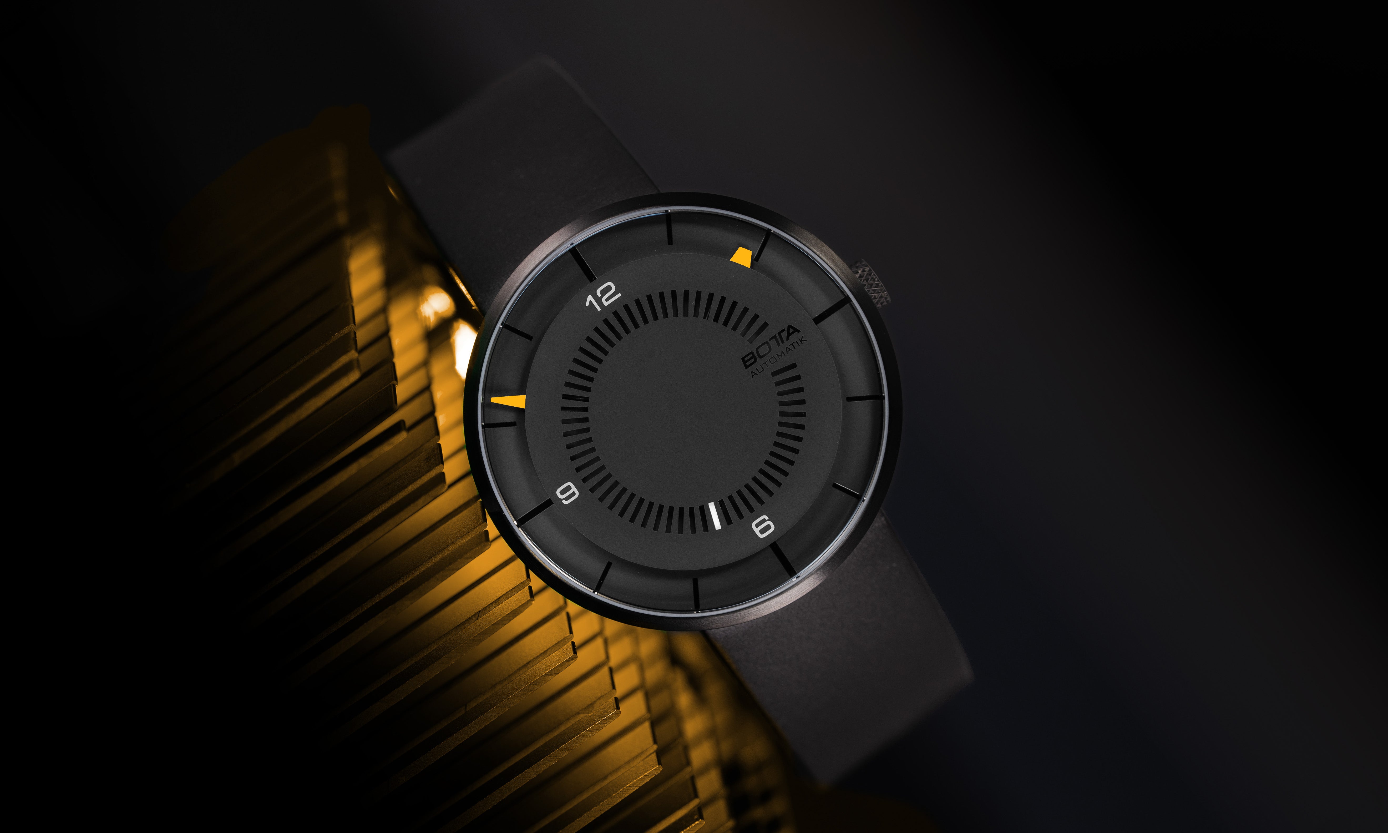 Die BOTTA CLAVIUS Automatik 44 mm ist eine preisgekrönte Designuhr, die futuristische Eleganz verkörpert. Im Bild liegt die Automatikuhr mit schwarzem Zifferblatt und auffällig leuchtenden Zeigerspitzen in Orange und Weiß, die wie Lichtpunkte auf dem reduzierten Zifferblatt wirken. Das Titangehäuse mit Saphirglas macht diese besondere Automatikuhr robust und leicht. Eine exklusive Armbanduhr für Liebhaber, die eine außergewöhnliche Automatikuhr kaufen oder bestellen möchten.