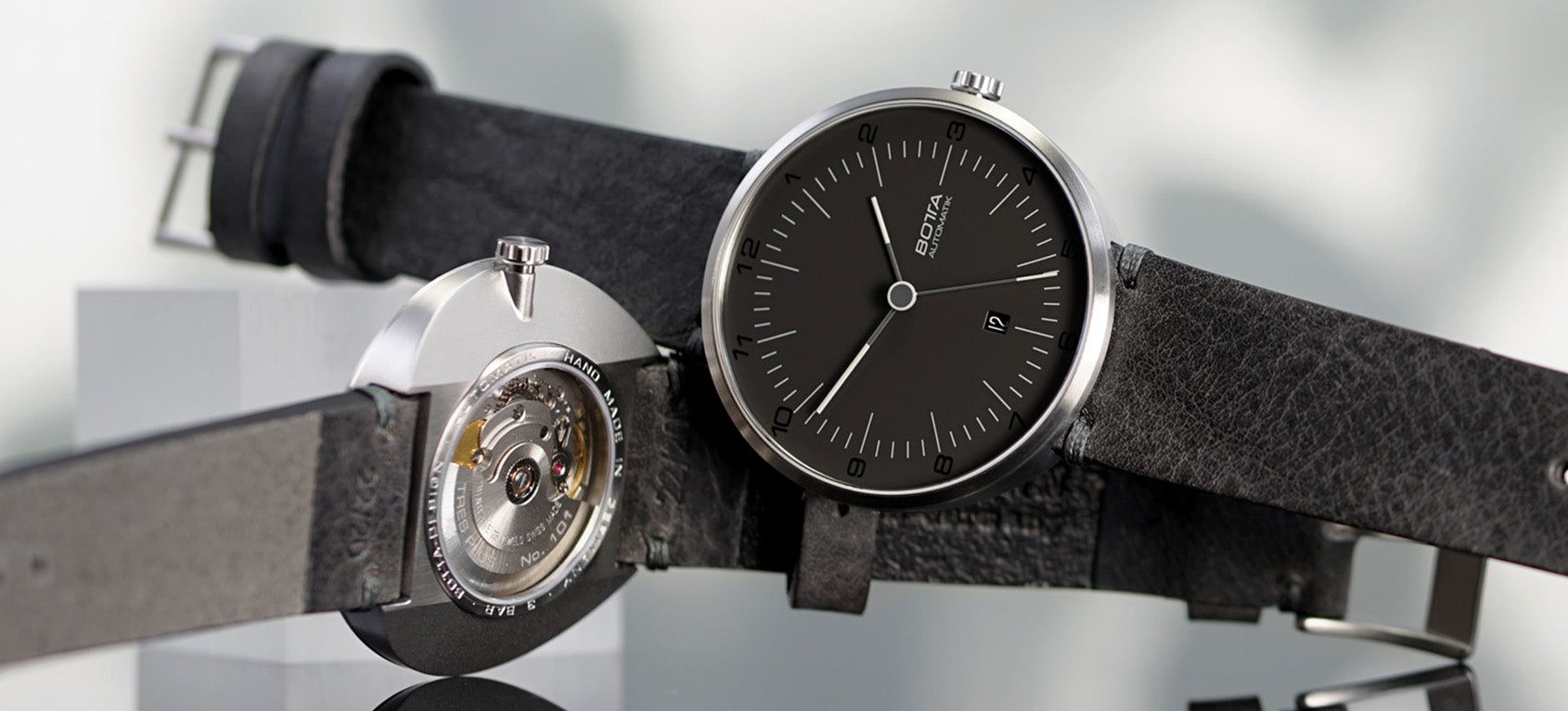 Abgebildet ist die TRES Automatik von BOTTA Design mit schwarzem Zifferblatt. Das 44 mm Titangehäuse beherbergt das präzise Sellita SW200-1 Automatikwerk, sichtbar durch den transparenten Gehäuseboden. Die klare Gestaltung mit Dreizeigeranzeige und Datum unterstreicht den Bauhaus-inspirierten Purismus. Diese Automatikuhr ist eine moderne Designuhr und stilvolle Armbanduhr – perfekt für Individualisten, die eine hochwertige Uhr kaufen oder bestellen möchten.
