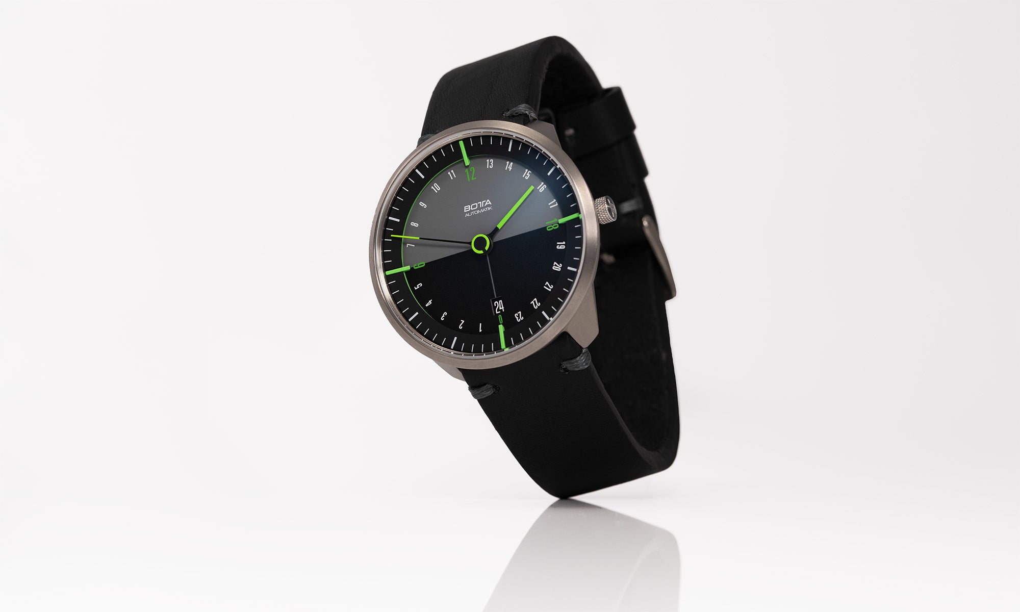 Die TRES 24 Automatikuhr von BOTTA Design ist eine außergewöhnliche Designuhr und zugleich eine innovative Einzeigeruhr mit zusätzlichem Minuten- und Sekundenindikator. Auf dem Bild ist die elegante Armbanduhr mit schwarzem Zifferblatt, grünen Applikationen und einem klaren 24-Stunden-Anzeigeprinzip zu sehen. Diese hochwertige Automatikuhr kaufen heißt, sich für inspiriertes Design und Logik am Handgelenk zu entscheiden.